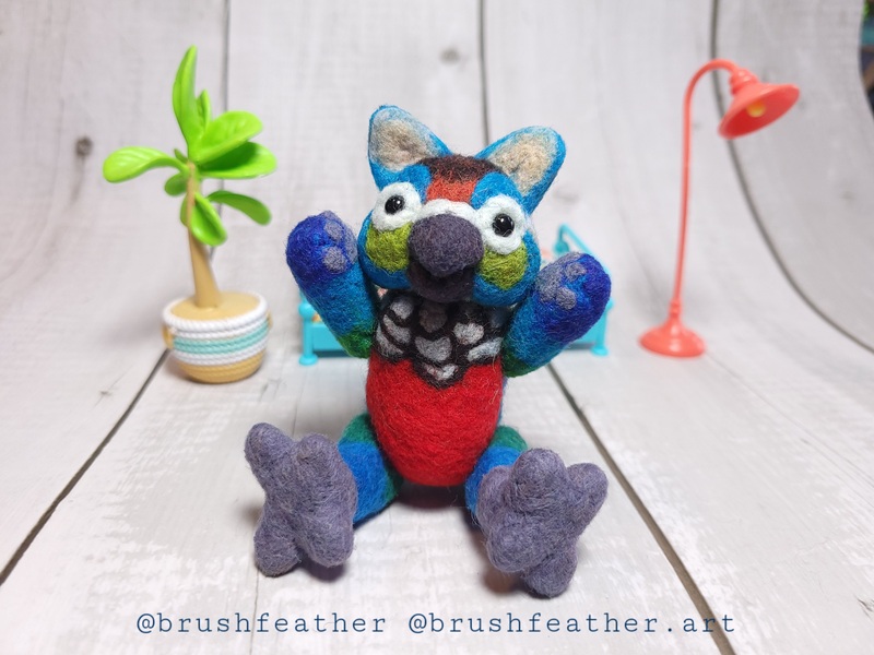 A string-jointed, needle-felted gryphon doll colored like a crimson bellied conure. They are sitting on the floor with their arms in the air - hooray! 